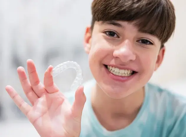 Smiling teen boy holding clear Invisalign aligner tray in his hand.