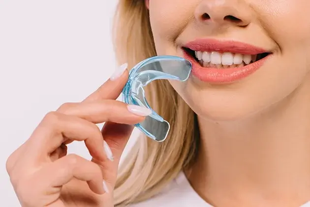 Woman holding a clear dental night guard while smiling, showing teeth alignment care.
