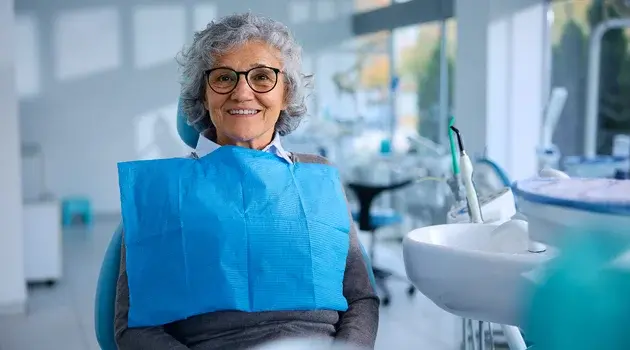 Smiling female endodontist wearing glasses and blue protective bib in modern dental office.