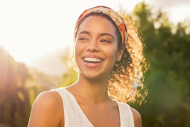 Young woman smiling brightly in natural sunlight, showcasing healthy teeth and a radiant cosmetic smile.